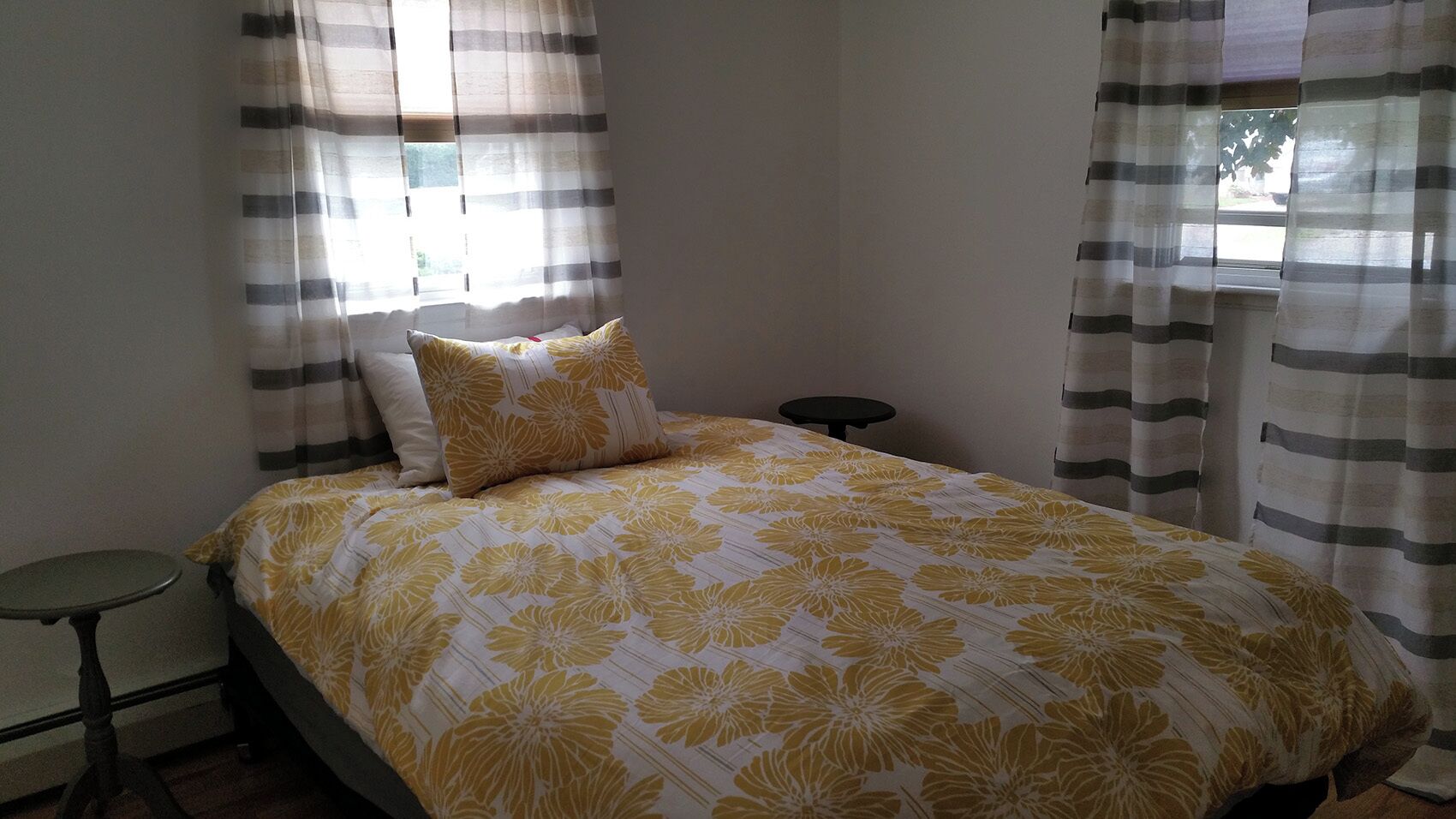 A bed with a floral bedspread, a pillow, a small round table, and curtains.