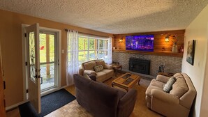 Ein Wohnzimmer mit Kamin, einem an der Wand befestigten Fernseher und einer Tür zum Patio.