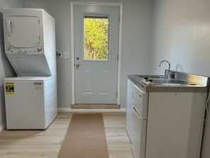 A compact kitchen with a built-in washer and dryer, a small sink, and a door with a view of greenery.