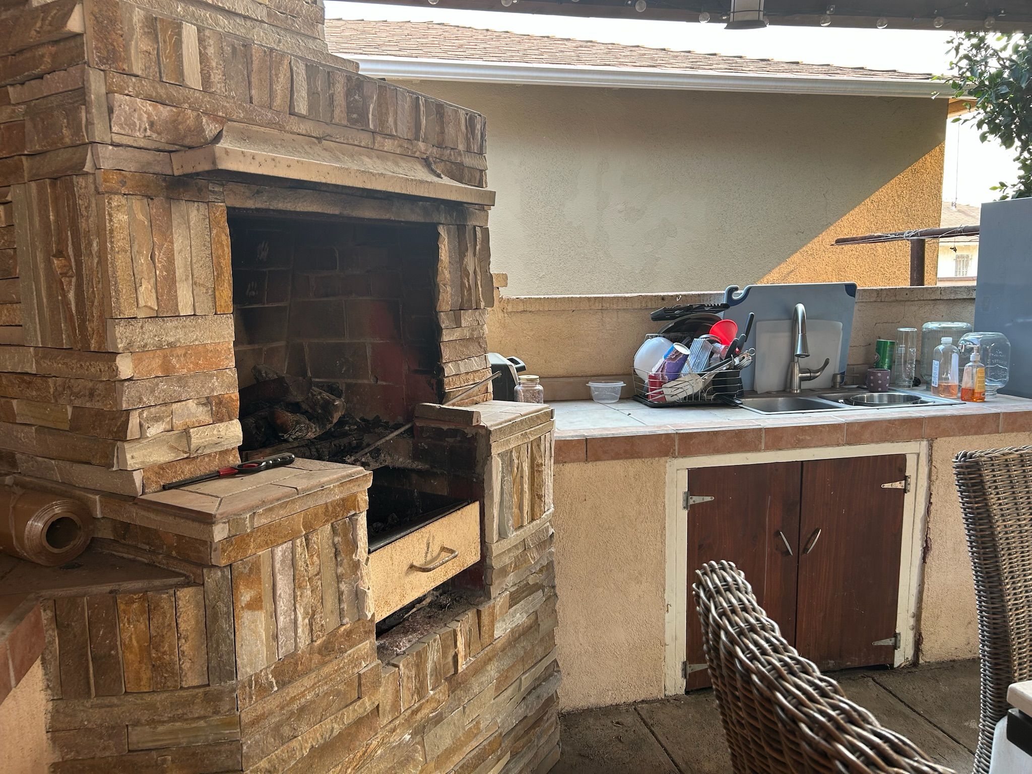 An outdoor kitchen with a stone-built grill, a sink, and a wicker chair.