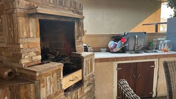 An outdoor kitchen with a stone-built grill, a sink, and a wicker chair.