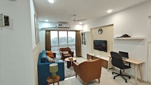 A modern living room with a sofa, armchair, coffee table, TV, and desk with a computer. - Terrific 2-bedroom apartment with AC in vibrant Mumbai (Mumbai)
