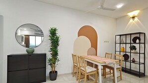 A dining area with a table, chairs, a potted plant, a black cabinet, a mirror, and a wall-mounted shelf with decorative items. - Terrific 2-bedroom apartment with AC in vibrant Mumbai (Mumbai)