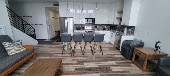 Eine moderne Küche mit weißen Schränken, einem Edelstahlkühlschrank und einem Essbereich mit Holztisch und -stühlen.