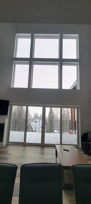 Ein Zimmer mit einem großen Fenster, einem Holztisch und grünen Stühlen.