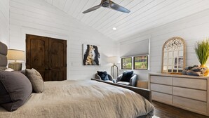 Ein Schlafzimmer mit einem großen Bett, einem Deckenventilator, einer Holztür, einem Gemälde, einer Kommode und einem Fenster mit Blick.