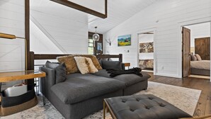 Ein modernes Loft mit einem grauen Ecksofa, einem Lederhocker und einem Holzesstisch.
