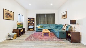 Ein Wohnzimmer mit Ecksofa, Fernseher, Bücherregal und einem gemusterten Teppich.