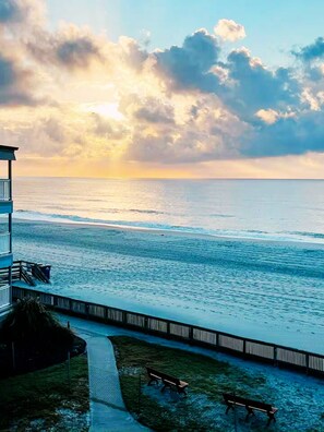 A coastal view with a wooden pier, a bench, and a building with a balcony overlooking the ocean. - Sunrise Shores // Myrtle Beach (Myrtle Beach)