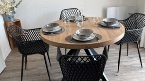 Ein runder Holztisch mit schwarzen Mesh-Stühlen, einer an der Wand befestigten Uhr und gerahmten Bildern.