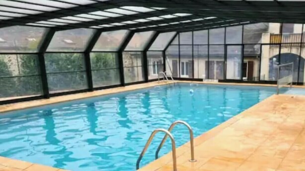 Ein Hallenbad mit klarem, blauem Wasser, gefliestem Boden und einer Glasüberdachung.