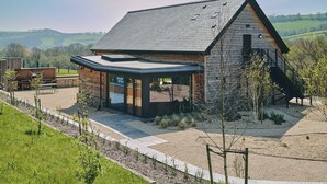 A modern house with a sloped roof, a covered patio, and a stone exterior. - Grain Loft - Luxury Cottages (Caersws)