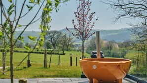 A large terracotta planter with a metal pole, set on a stone patio with a view of a rural landscape. - Grain Loft - Luxury Cottages (Caersws)