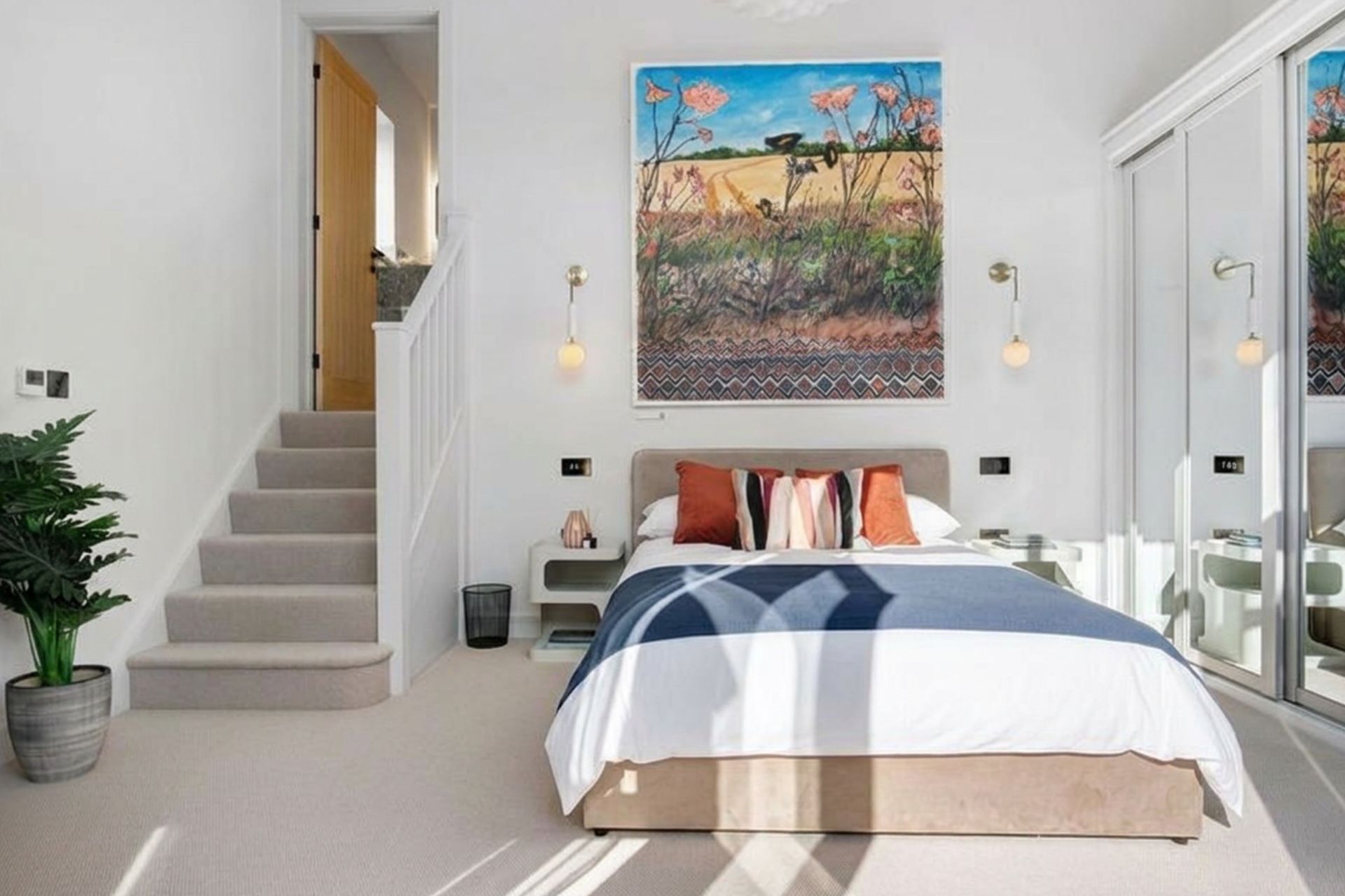 A bedroom with a bed, a painting, a staircase, and a plant.