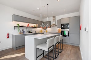 Una cocina moderna con una isla central, taburetes de bar, iluminación colgante y electrodomésticos integrados.