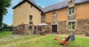 Ein Steinhaus mit einer großen, offenen Terrassenfläche, einem Holzstuhl und einem Tisch mit Sonnenschirm.