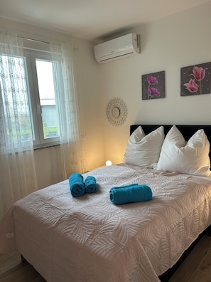 A hotel room with a bed, white pillows, a wall-mounted air conditioner, and two flower paintings. - Luxurious new 3-room apartment with lake views and a pool on Lake Garda in Peschiera (Boschetti)