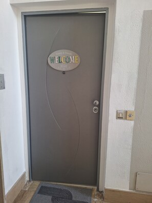 A door with a 'WELCOME' sign, a doorknob, and a light switch on the wall. - Spacious 4-bedroom apartment in tranquil Riva del Garda with AC (Riva del Garda)