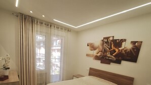 Ein Schlafzimmer mit einem großen Bett, einem Nachttisch, einer Kommode und einem Fenster mit Vorhängen.