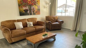 A living room with a brown leather sofa, a matching armchair, a wooden coffee table with a plant, and a painting of flowers on the wall. - Puppy play pen 2-bedroom house with AC in sunny Phoenix (Phoenix)