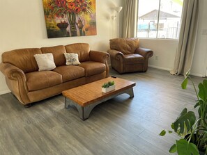 Ein Wohnzimmer mit braunem Ledersofa, einem passenden Sessel, einem Holztisch mit einer Pflanze und einem Blumenbild an der Wand.