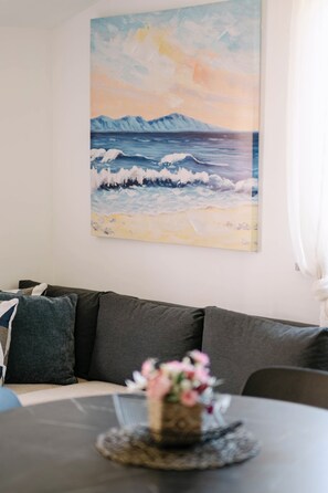 Ein Wohnzimmer mit einer Couch, einem Couchtisch mit Blumen in einer Vase und einem Gemälde einer Strandlandschaft an der Wand.