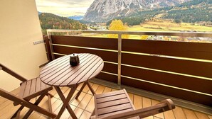 En balkon med et træbord og stole, med udsigt over et bjergrigt landskab.