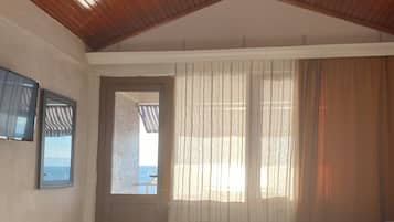 A bedroom with a wooden ceiling, a bed, a window with curtains, and a door.