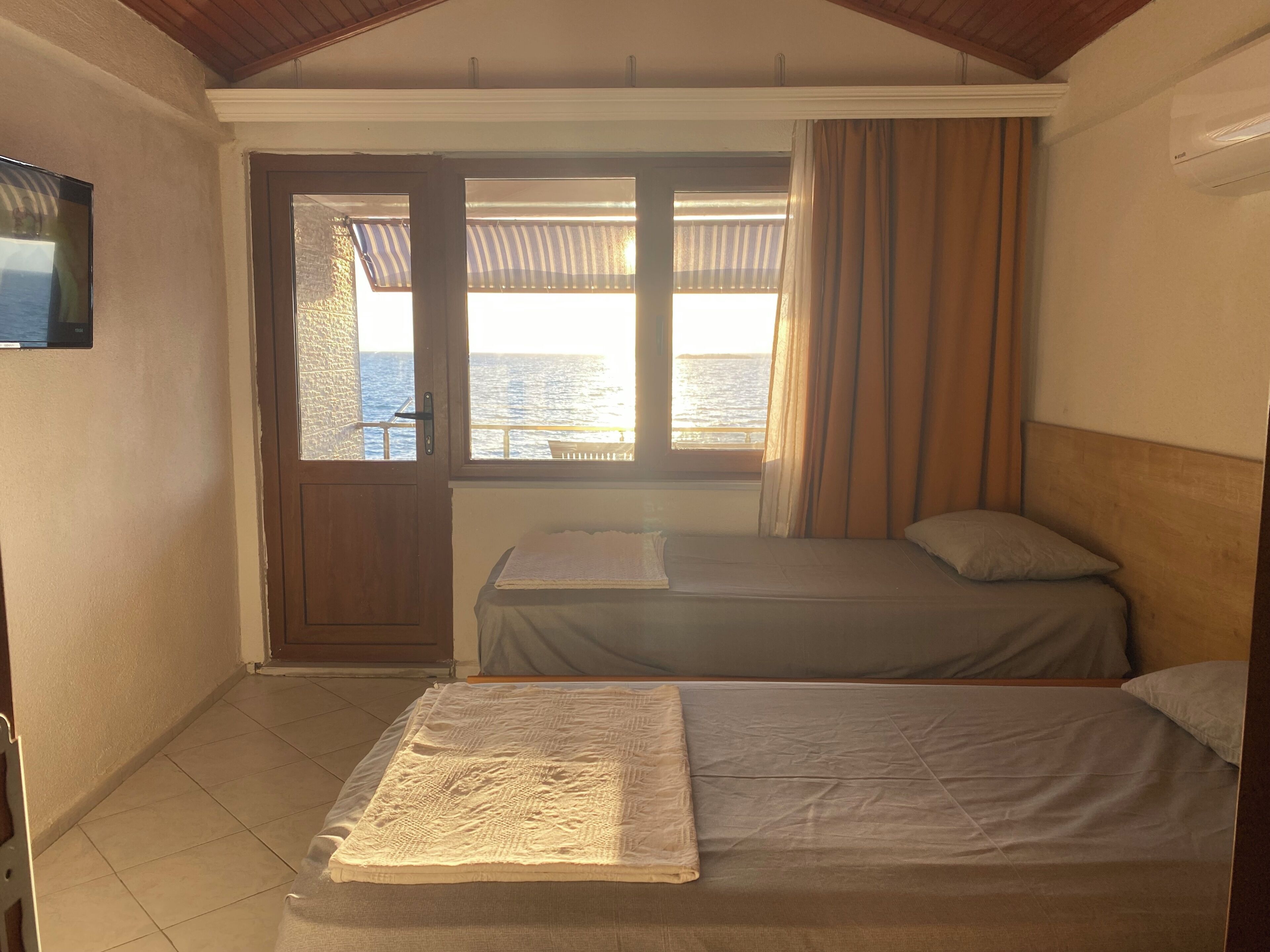 A room with two beds, a television, a window with curtains, and a view of the sea.