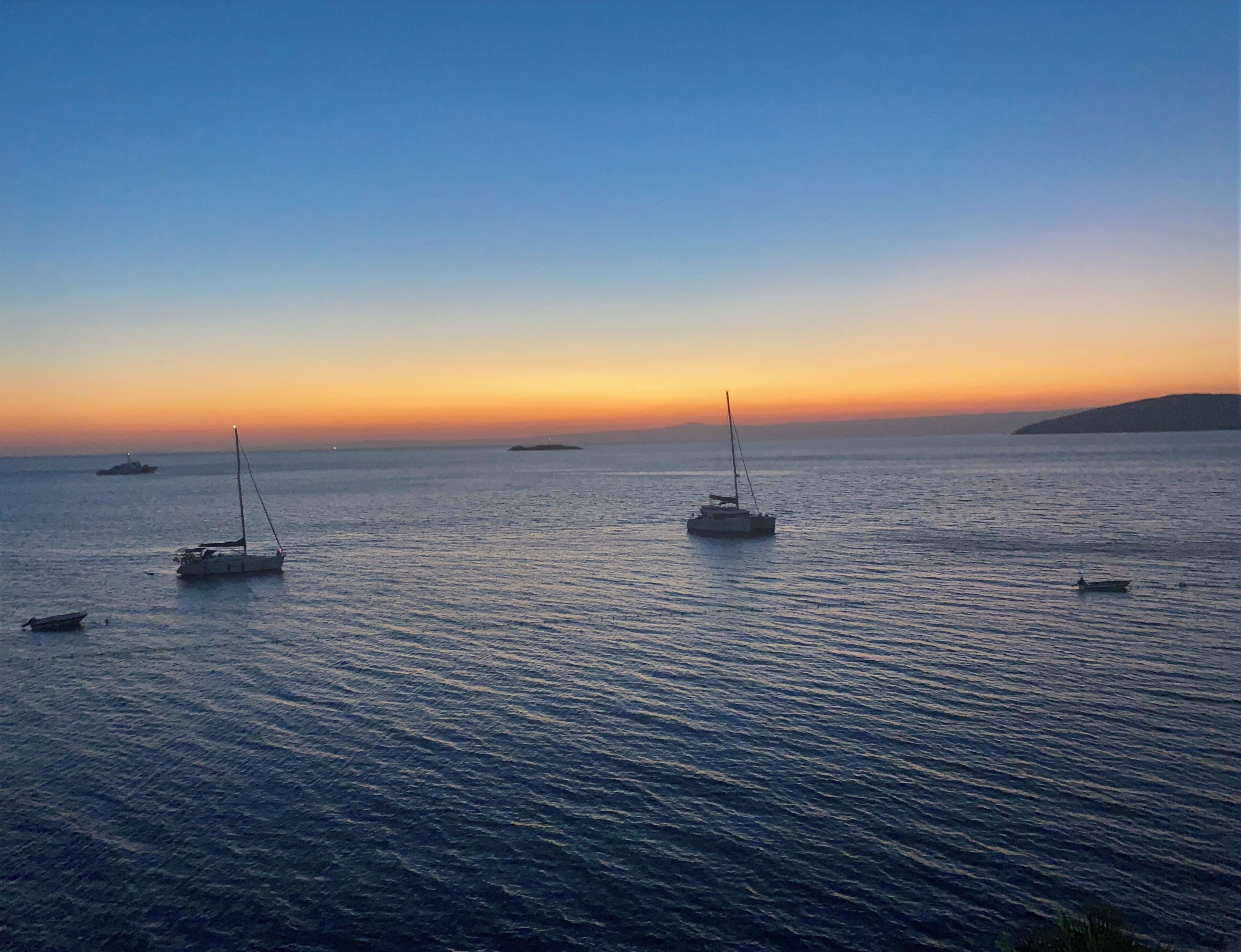 A calm sea at sunset with several boats.