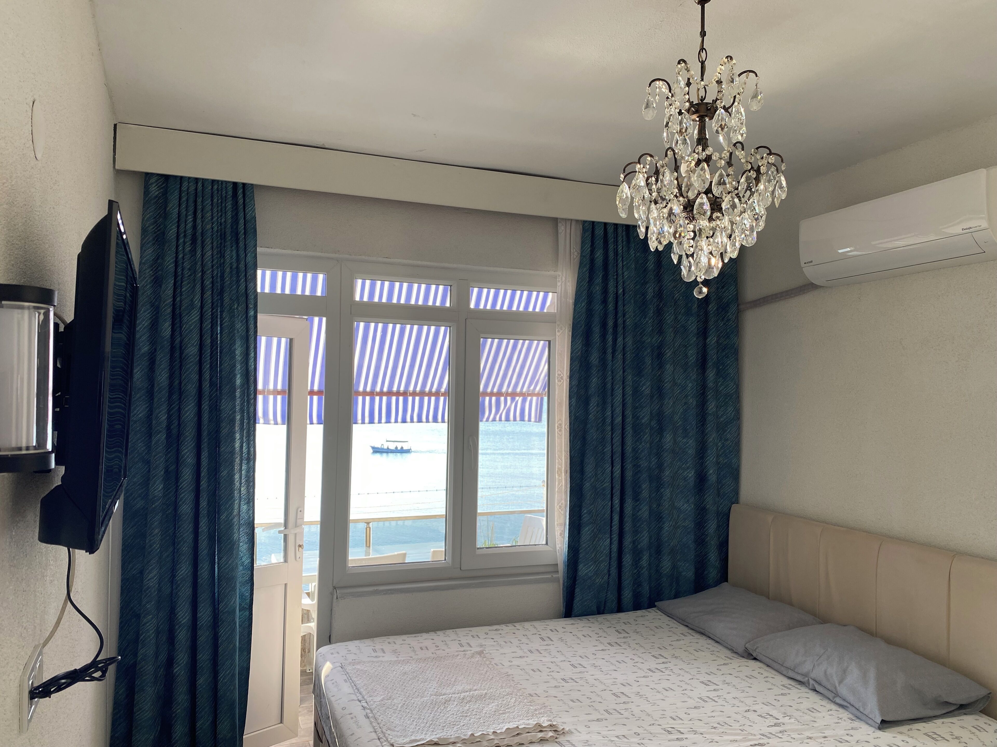Une chambre à coucher avec un lit, un lustre, une télévision et une vue sur la mer par la fenêtre.