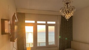 A bedroom with a bed, a chandelier, a TV, and a window with a view of the sea. - Lavin Suit (Marmara)