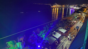 Un hotel frente al mar con vistas al océano, asientos exteriores y una zona cubierta con palmeras.