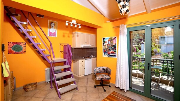 A bright orange room with a staircase, a kitchen, a dining area, and a sliding glass door to an outdoor patio. - Cleo Apartment - Quaint Loft in Kefalonia (Kefalonia)
