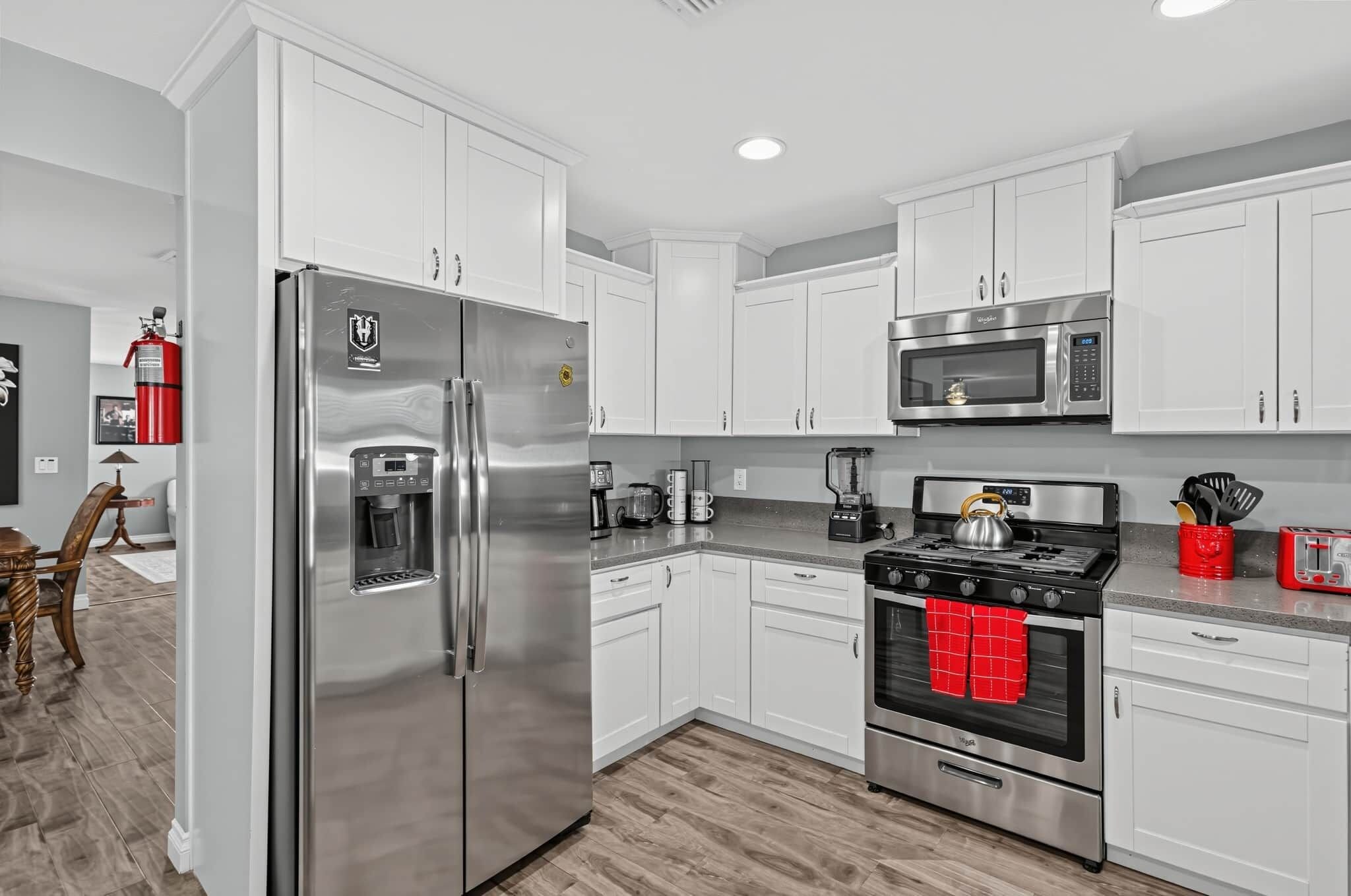 A modern kitchen with stainless steel appliances, white cabinetry, and a wood floor.