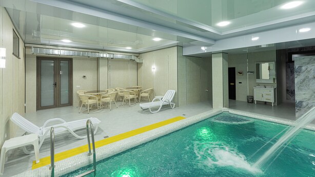 An indoor swimming pool with lounge chairs, a table, and chairs, and a small bathroom area. - Boutique Hotel IMONA (Samarkand)