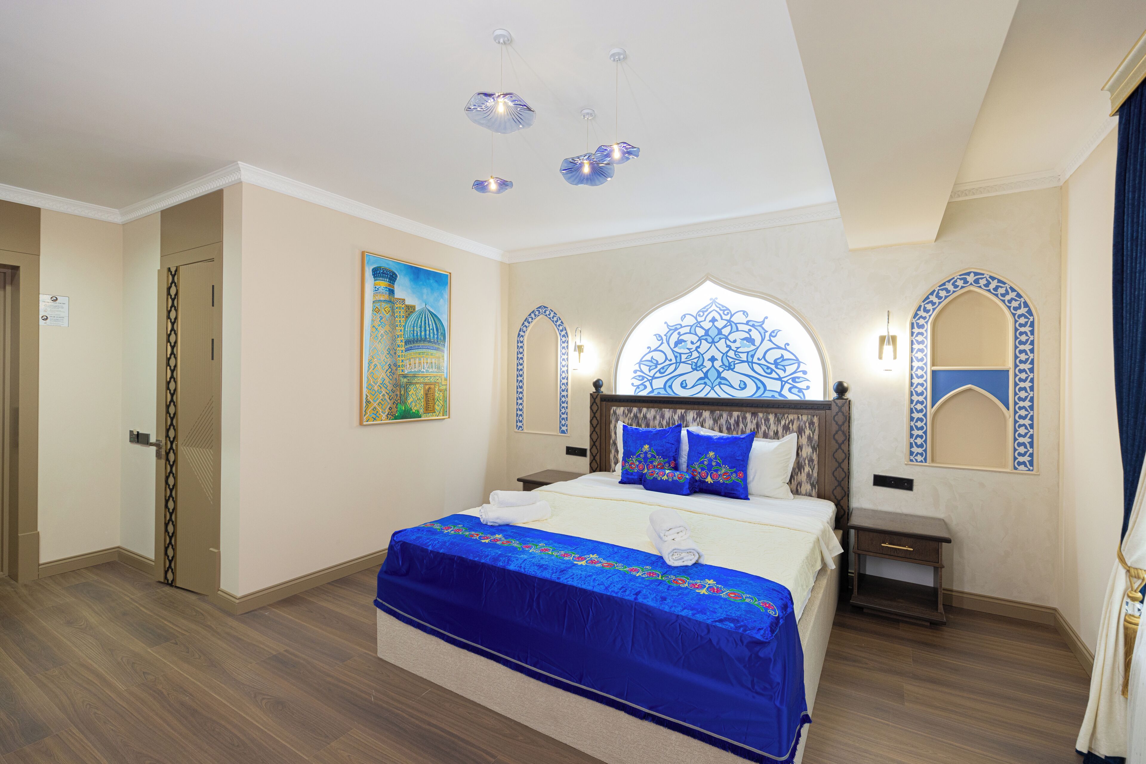 Quarto de hotel com uma cama grande, uma mesa de cabeceira, um espelho fixado na parede e uma porta.