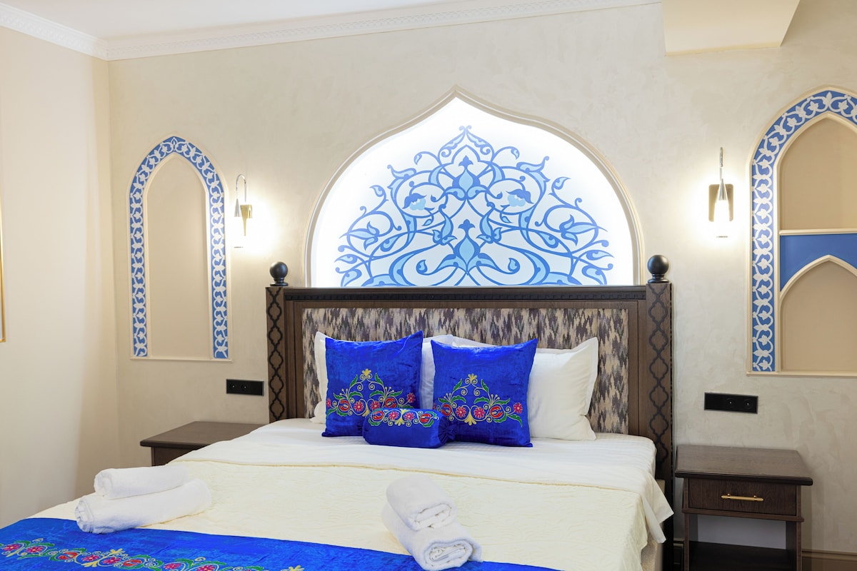 Une chambre d’hôtel comprenant un lit, deux tables de chevet, une arche décorative sur le mur et un luminaire fixé au mur.