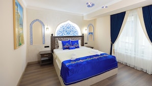 A hotel room with a large bed, a nightstand, a bedside table, a decorative wall arch, and a window with curtains. - Boutique Hotel IMONA (Samarkand)