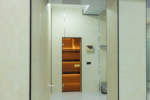 A hallway with a wooden door, a trash bin, and a digital display. - Boutique Hotel IMONA (Samarkand)