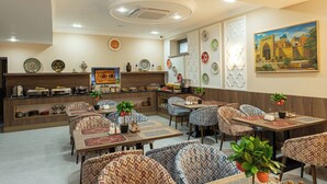 A restaurant with a central counter, multiple dining tables with patterned chairs, decorative plates on the walls, and a painting. - Boutique Hotel IMONA (Samarkand)