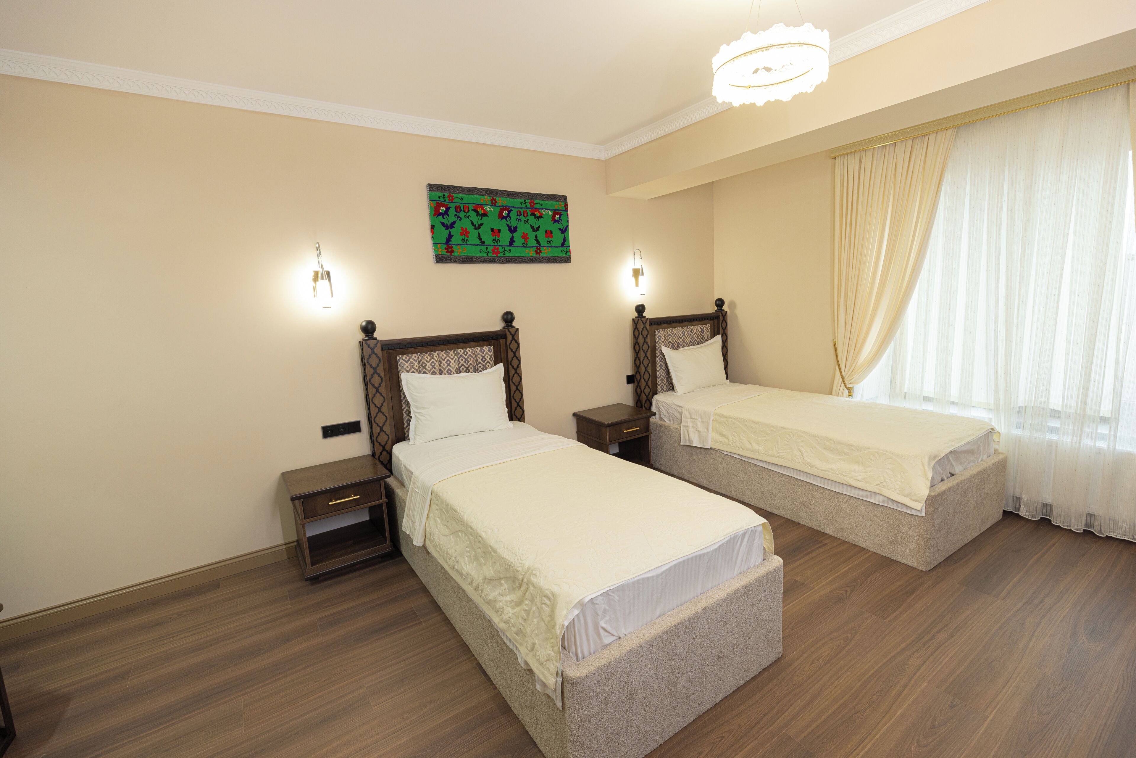 A hotel room with two beds, a nightstand, a wall-mounted artwork, and a window with curtains.