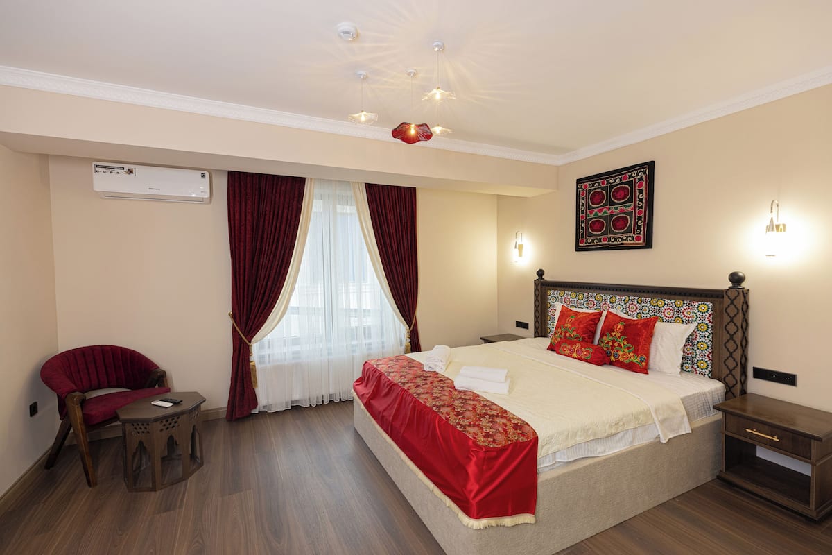 Une chambre d’hôtel comprenant un lit, une chaise, une petite table, une table de chevet, un appareil de climatisation et une fenêtre avec des rideaux.