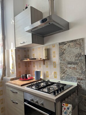 Eine Küche mit Gasherd, Backofen und einer Dunstabzugshaube aus Edelstahl. Der Spritzschutz besteht aus gemusterten Fliesen und an der Wand ist ein Steinakzent.