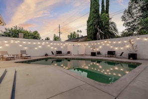 A swimming pool with string lights, lounge chairs, and a white brick wall. - Fully Equipped ADU Close to Business Centers, Hospital Centers, & Attractions (Los Angeles)