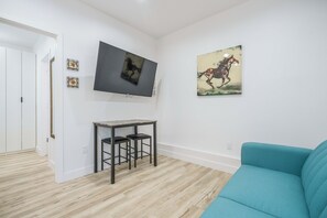 A room with a flat-screen TV mounted on the wall, a small table with two chairs, a teal sofa, and two framed pictures. - Fully Equipped ADU Close to Business Centers, Hospital Centers, & Attractions (Los Angeles)