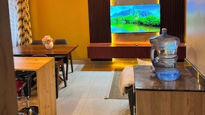 A modern living room with a flat-screen TV, wooden furniture, and pendant lighting. - Ocean Blue cozy airbnb with pool/gym. Perfect for relaxing and staying active. (Kampala)