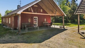 Un bâtiment rouge avec un toit en bois, un banc et une table à l’extérieur.