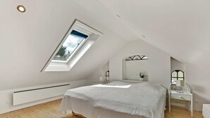 Une chambre avec un plafond en pente, un puits de lumière, un lit, une table de chevet et une étagère fixée au mur.