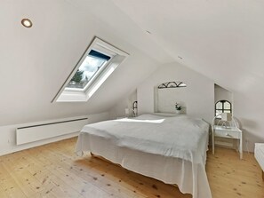 Ein Schlafzimmer mit schrägem Dach, einem Oberlicht, einem Bett, einem Nachttisch und einem an der Wand befestigten Regal.